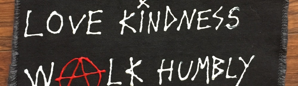Square black canvas patch. Handwritten in white puffy paint “Do Justice, Love Kindness, Walk Humbly – Friendly Anarchism”